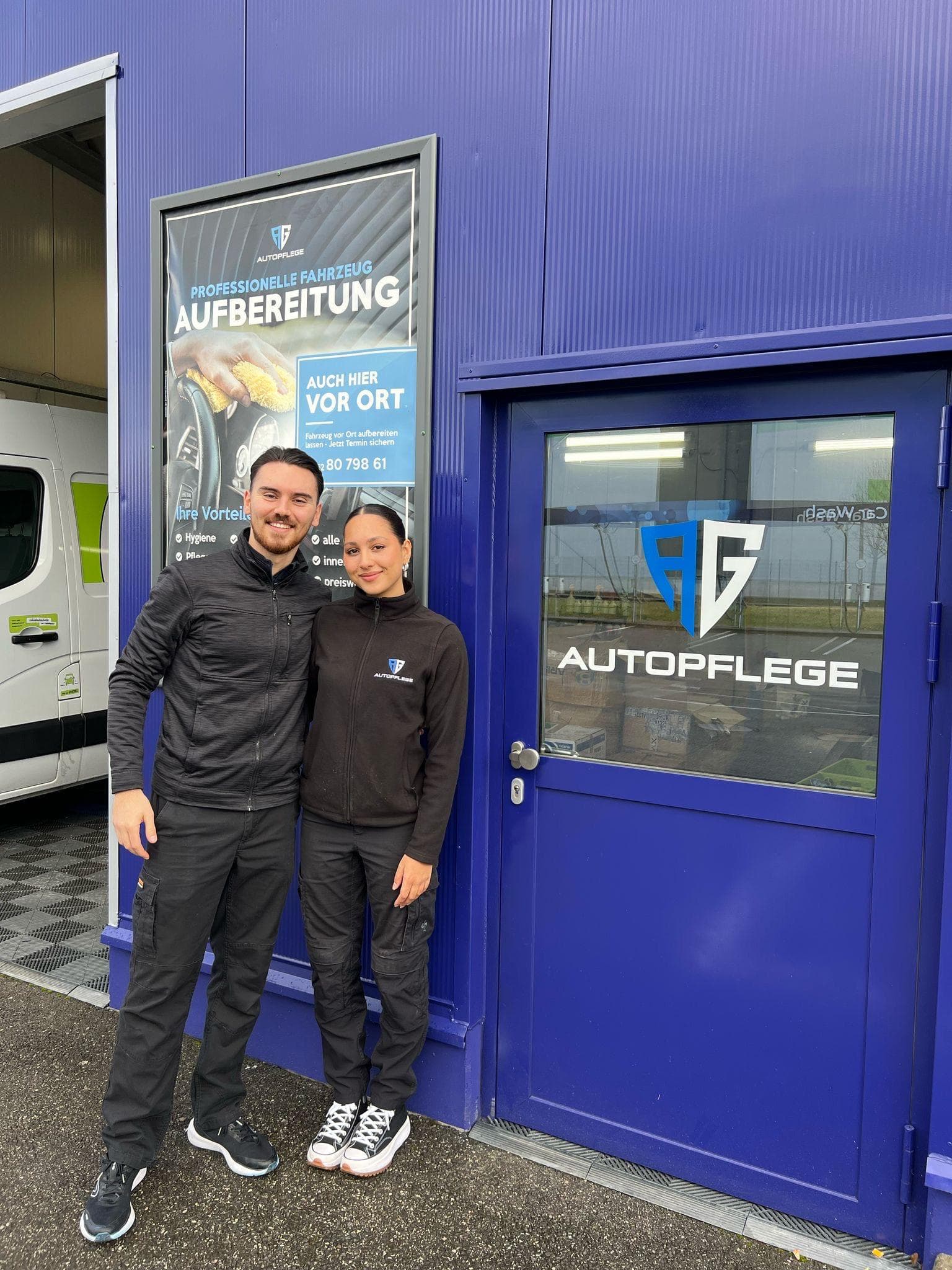 Ardonis Gashi und Alisha Baumann in Arbeitskleidung vor der blauen Fassade von AG Autopflege