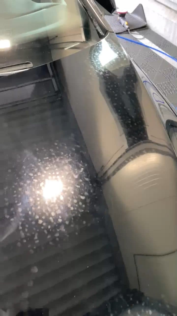 Schwarze Motorhaube mit vielen eingebrannten Kalkflecken im Licht der Hallenbeleuchtung